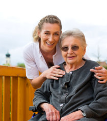 happy senior woman wearing glasses in wheelchair with a caregiver